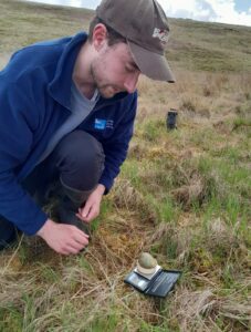 Andy Scott RSPB Geltsdale residential volunteer kneeling in an upland field beside small weighing scales with a Curlew egg on them.