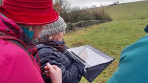 Two people holding a covered writing pad in a field, looking out over the field, during volunteer training at Hadrian's Wall © RSPB